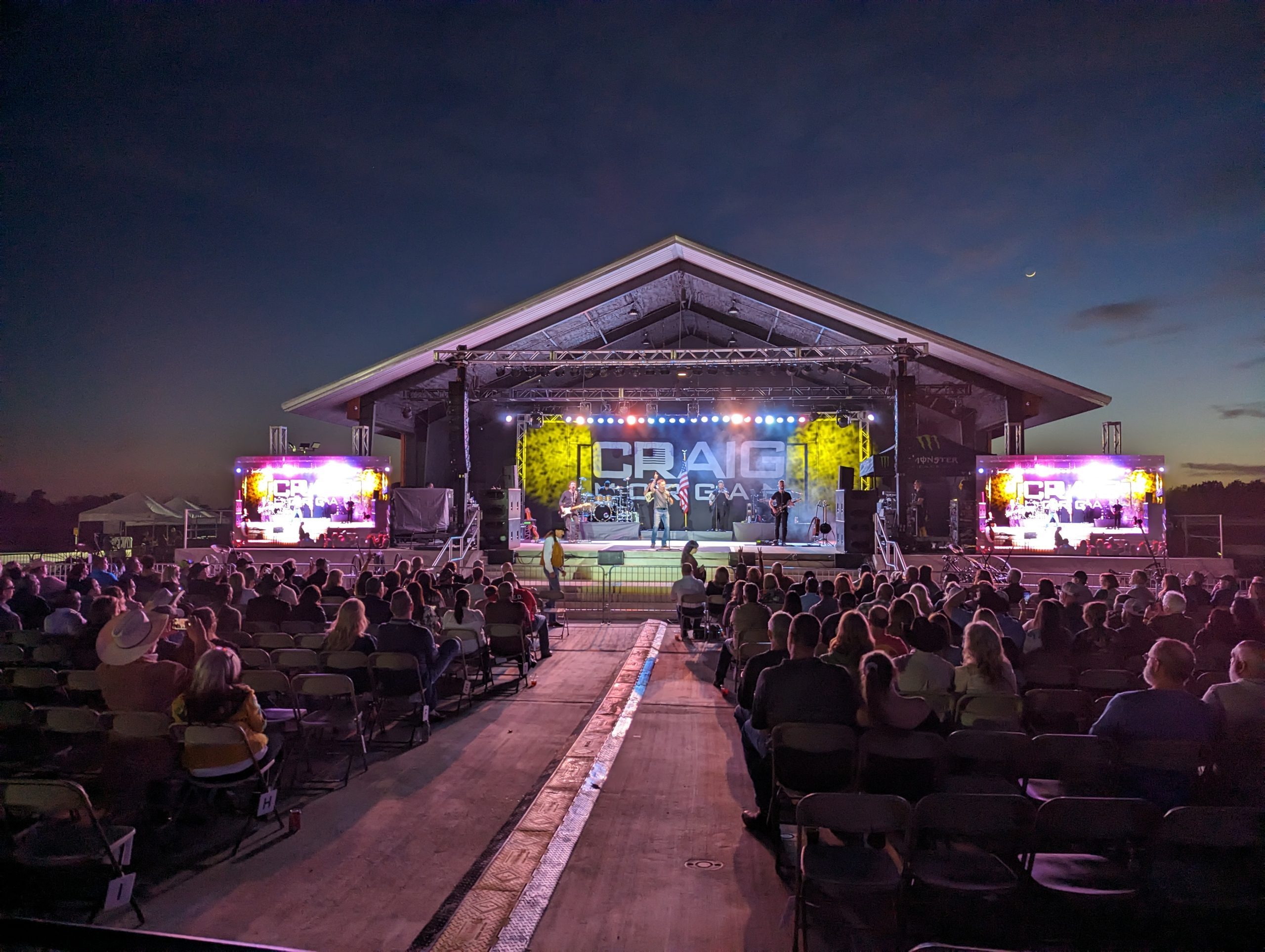 Steel-frame covered stage designed for outdoor use, fitted with rigging, lighting, and audio—raised high for better visibility and impact
